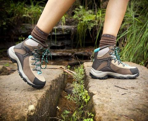 Fit young hiker crosses stone steps in hiking boots.