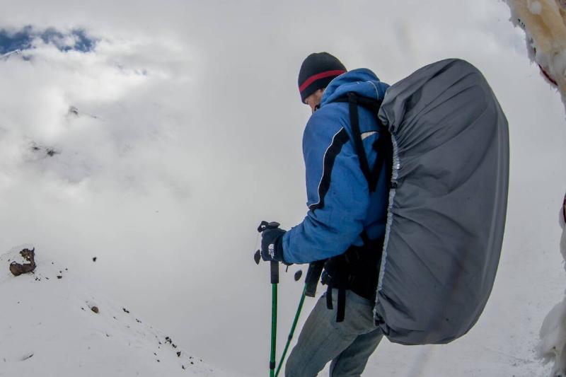 Backpacker in snow with pack covered by pack cover. 