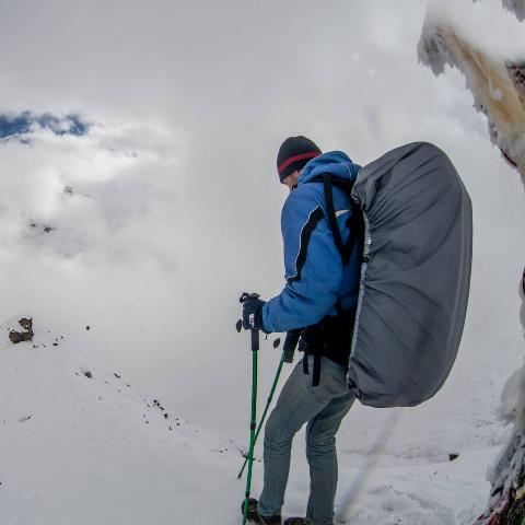 Backpacker in snow with pack covered by pack cover. 
