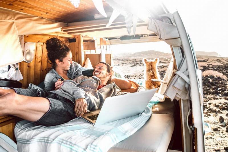 Two people laying in van together with a dog. 