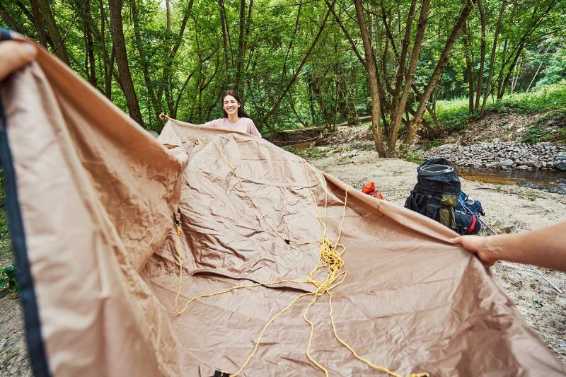 Woman and man putting up tarp tent in forest. 