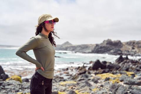 Woman wearing sunshirt and hat at a rocky beach. 