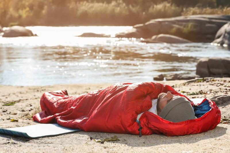 Man in sleeping bag on wild beach.