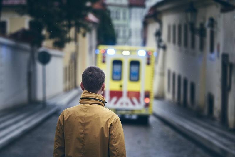 Man looking at leaving ambulance car of emergency medical service in rainy day.