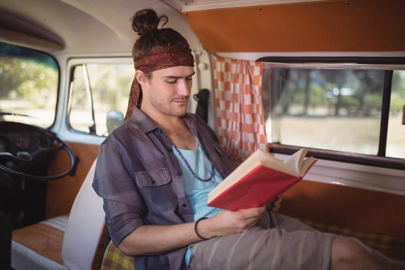 Young man reading book in mini van.