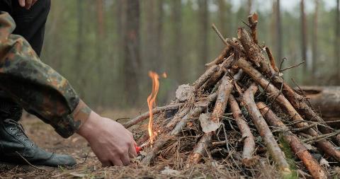 Man starts a fire in the forest using a lighter.