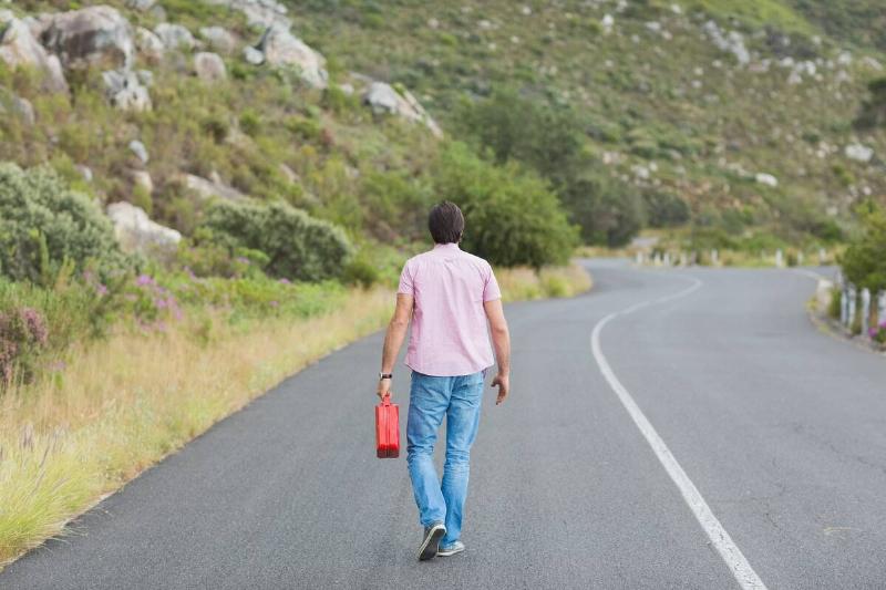 Man walking away holding petrolcan at the side of the road.