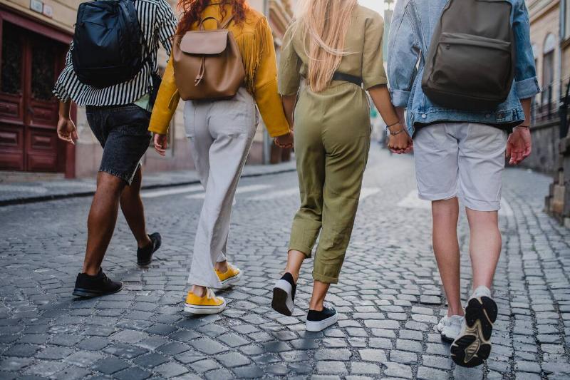 A rear view of group of young people outdoors on trip in town, walking and holding hands.