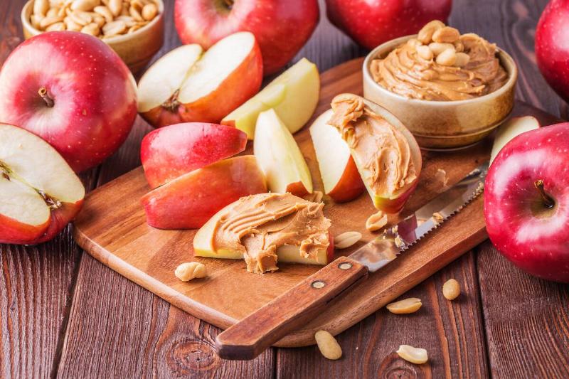 Red apples and peanut butter on a cutting board. 