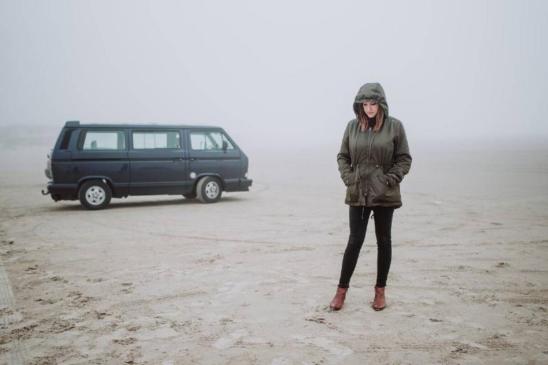 Woman standing in front of her van on an empty beach in winter time.