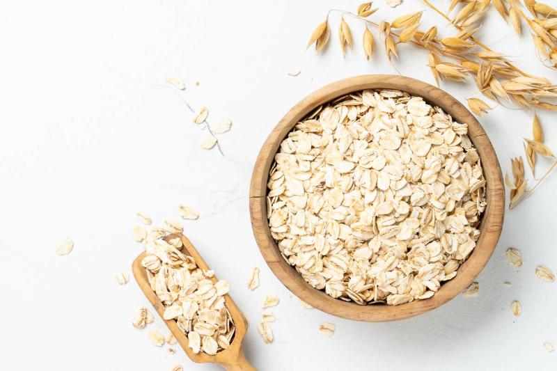 Rolled oats flakes in a wooden bowl with a wooden spoon. 