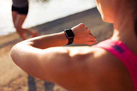 A woman looking at her smartwatch as she stands on the beach. 