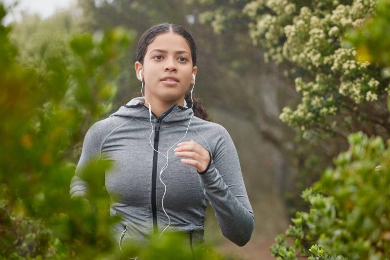 A young woman running in nature in a grey sweater. 