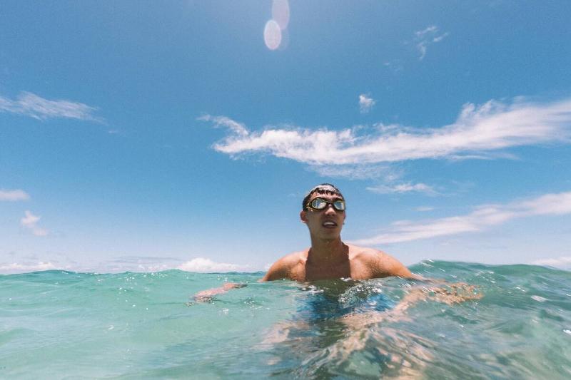 A man swimming in the ocean with goggles on his head. 