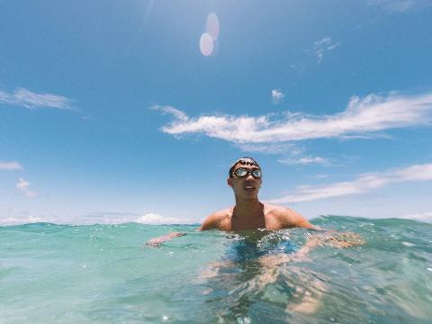 A man swimming in the ocean with goggles on his head. 