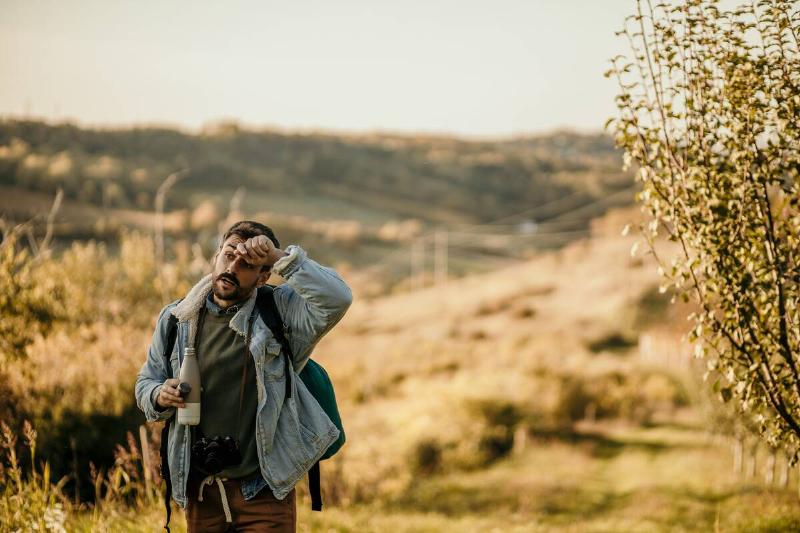 Man wiping sweat from forehead on hike. 