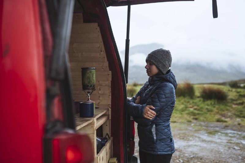 Woman using a portable camping stove to boil water in the back of her van.
