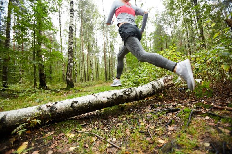 Woman jumping over a log in the forest. 