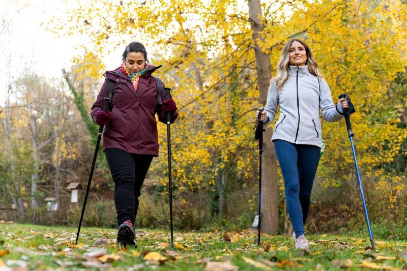 Two women walking with hiking poles in nature. 
