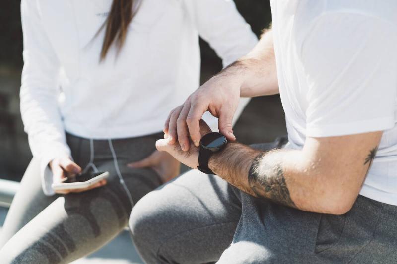 A man looking at a fitness tracker and a woman looking at the screen of her phone. 