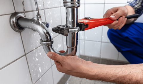 A plumber using a wrench on a pipe under a sink. 