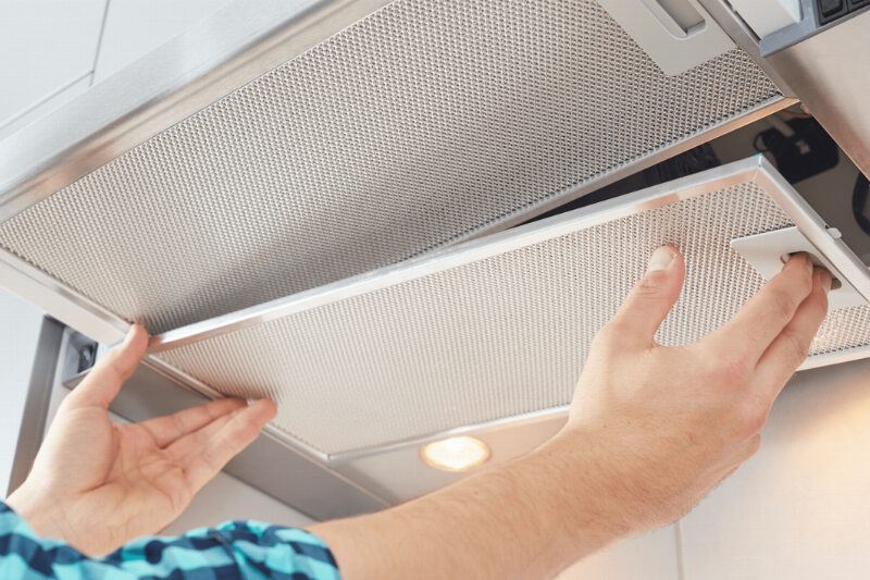 Hands removing the range hood filter.