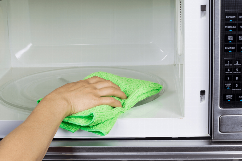 Wiping the inside of a microwave with a cloth.