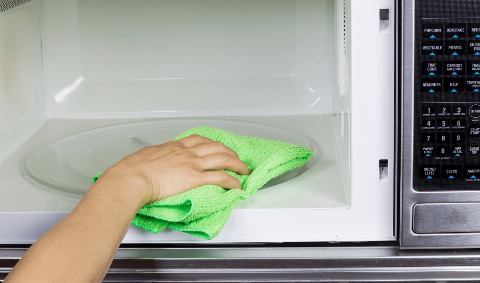 Wiping the inside of a microwave with a cloth.