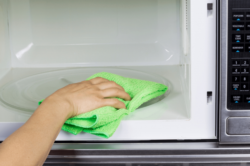 Wiping the inside of a microwave with a cloth.