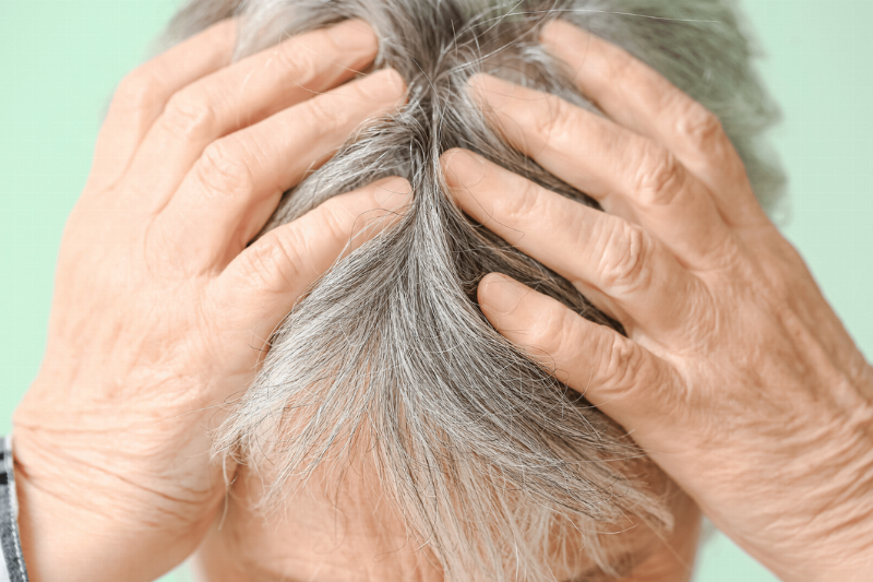A man with grey hair holding his scalp. 