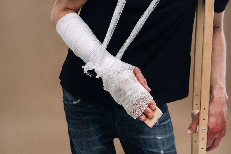 A man with a broken arm leaning on a crutch. 