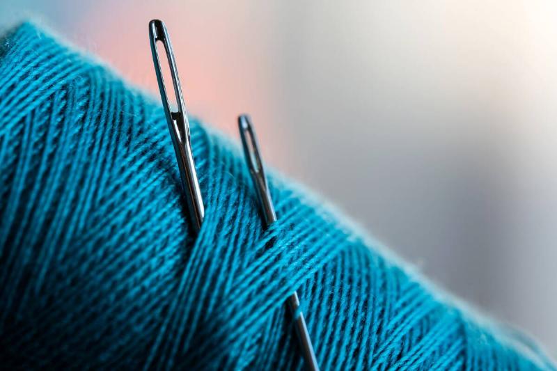 Two sewing needles tucked into blue thread. 