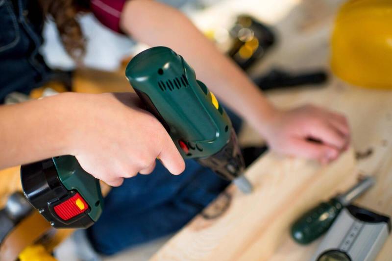 A girl using a power drill on wood. 