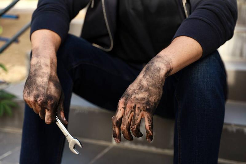 A mechanic with greasy hands holding a wrench. 