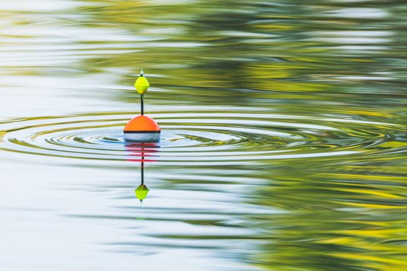 A fishing float floats on the water of the lake making circles in the water.