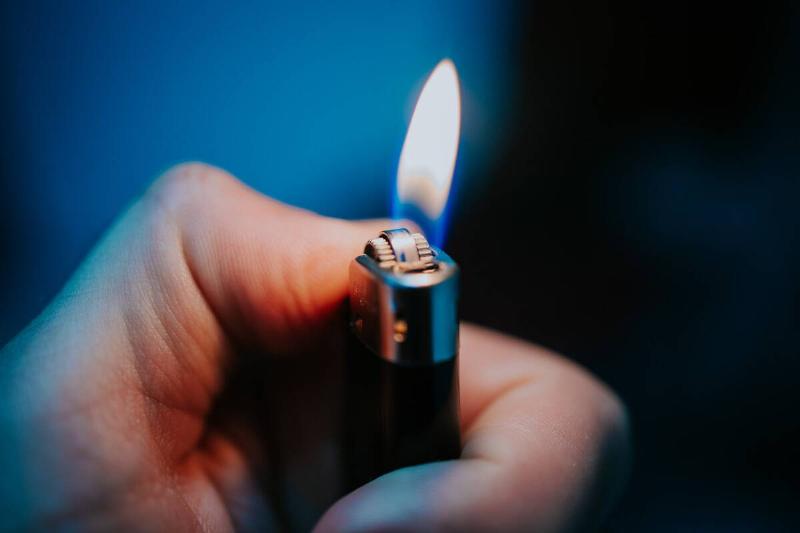 A male hand holding a flaming lighter.