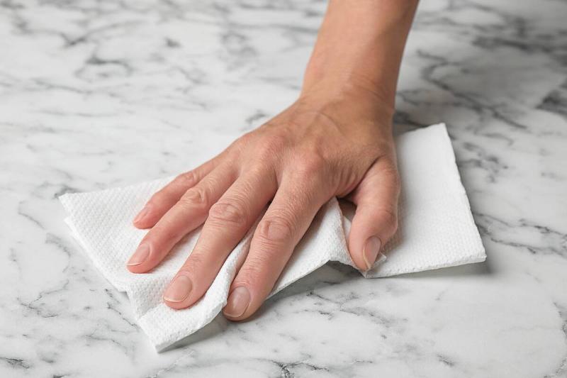 Hand wiping a marble countertop with a paper towel. 