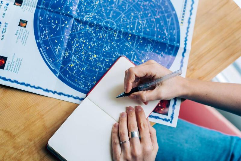 A hand writing notes next to an astronomy chart. 