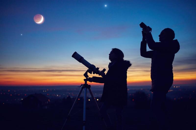 Two people using a telephone and camera at dusk. 