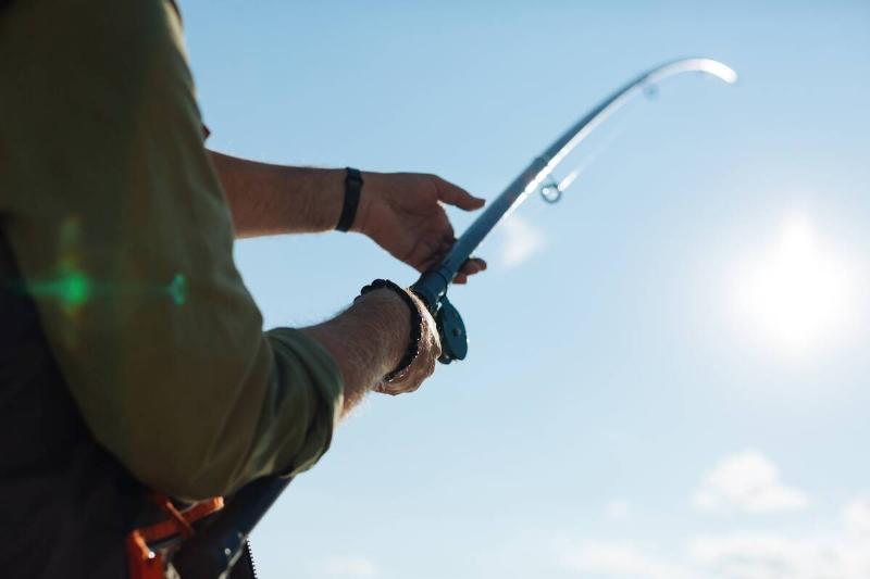Man holding a fishing rod in front of a blue sky. 