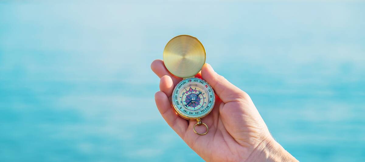 A hand holding a compass in front of the sea. 