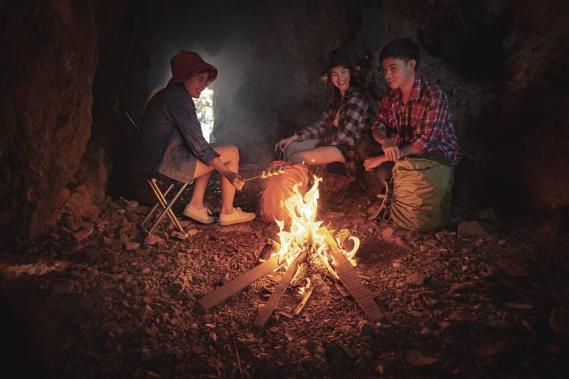 Three people sitting around a campfire in a cave. 