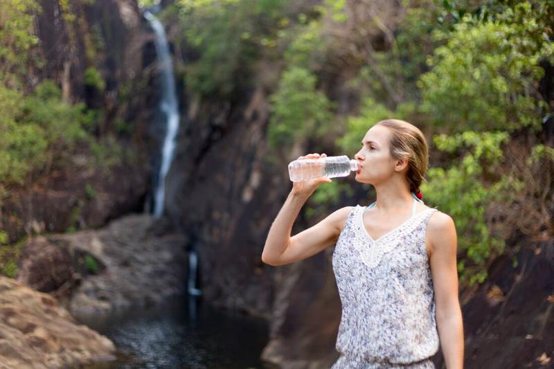 Girl drinks water from a bottle on the background of a waterfall.
