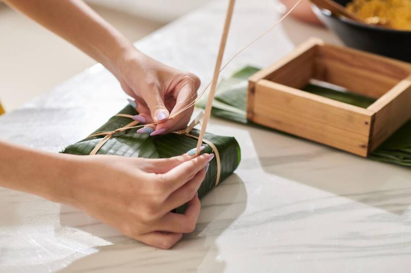 Hands of woman packing sticky rice cakes in banana leaves.