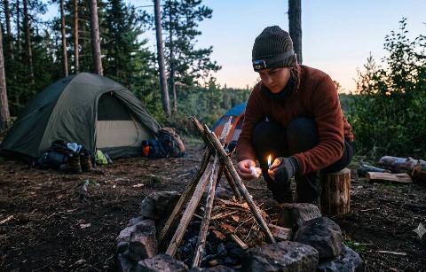 woman crouching in front of campfire pit, lighting cotton ball as fire starter