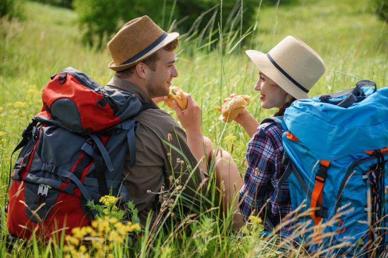 couple eating sandwiches seated while on a hike