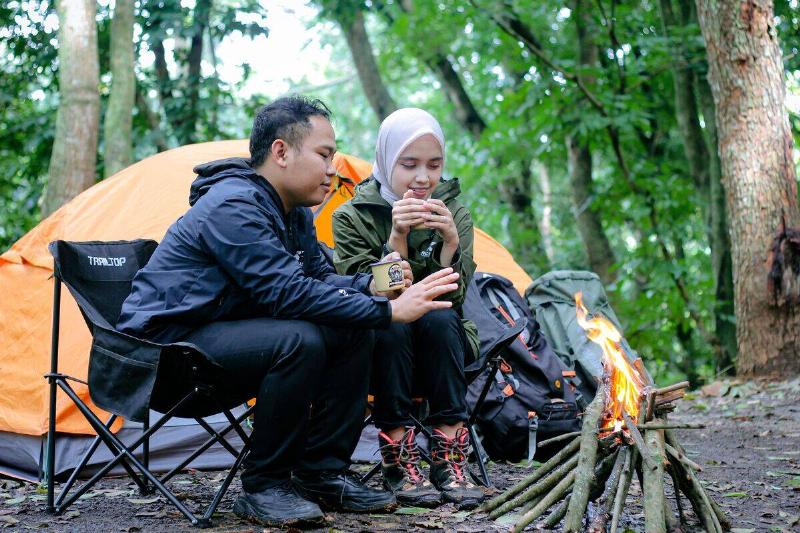 couple huddled around fire with orange tent behind them