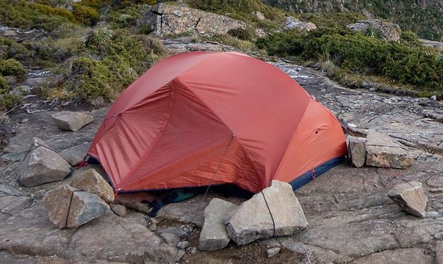 A modern two person, lightweight hiking dome tent; it is tied to rocks as there is nowhere to drive stakes on this rock shelf. Photo credit