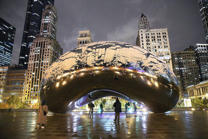 Individuals standing beneath the Bean at night