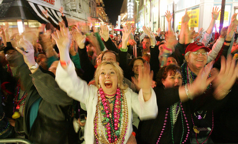 Crowd of people wearing Mardi Gras beads and holding their arms up